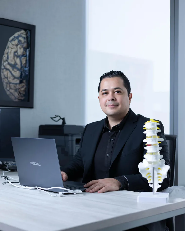 El Dr. Gerson Reyes en su escritorio junto a un modelo anatómico de columna lumbar