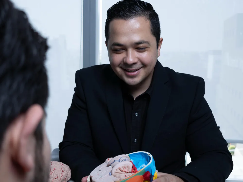 El Dr. Gerson Reyes explica a un paciente con un modelo anatómico de cerebro y cráneo